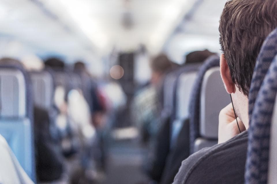 The aisle of a passenger plane, seen past a traveler in a window seat.