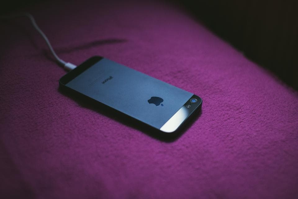A phone lying face down on a purple cloth with its charging cable plugged in.