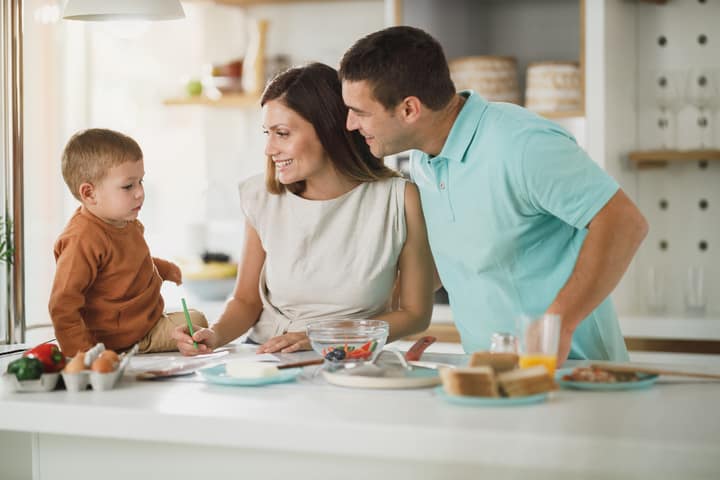 Two parents and a small child making breakfast together at a kitchen counter.