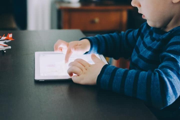 A child in a striped sweater tapping a tablet on a table.