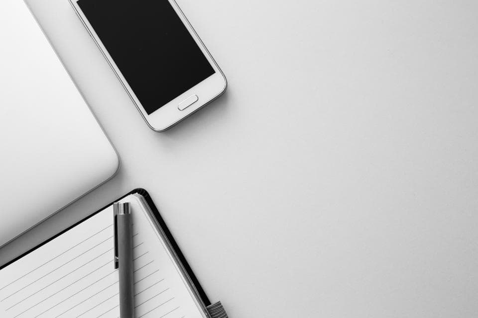 A white phone and an open notebook with a pen on a white desk.