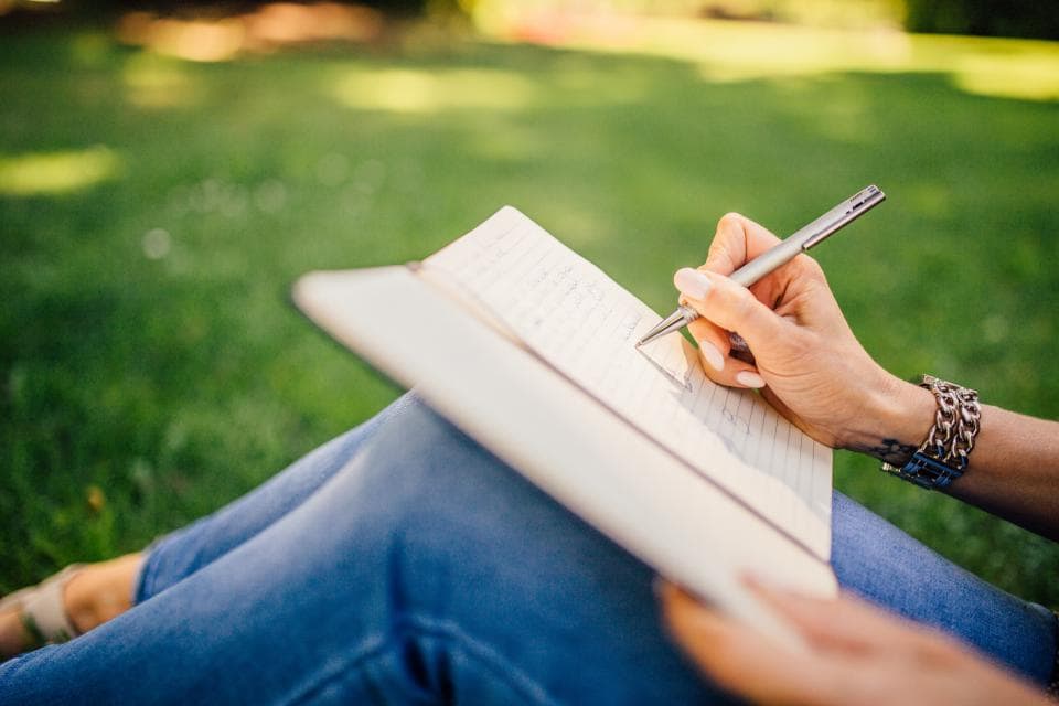A person sitting on the grass writing in a notebook.